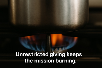 Close-up of a stainless steel pot on a gas stove with a steady blue and orange flame, symbolizing how unrestricted giving fuels nonprofit missions.